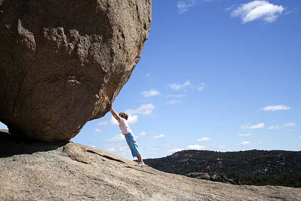 Photo of a person "pushing" a massive rock up a hill.