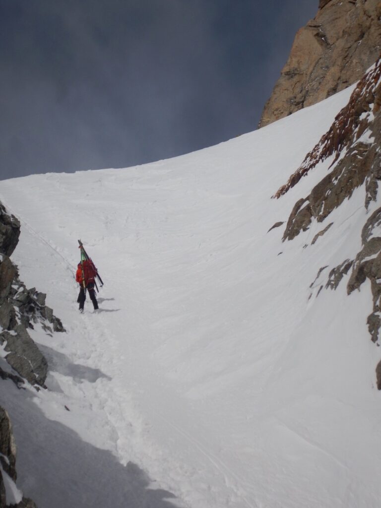 Packing skis up a steep, snowy mountain.