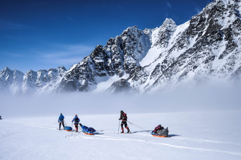 Pulling sleds across the snowy landscape in front of mountains.