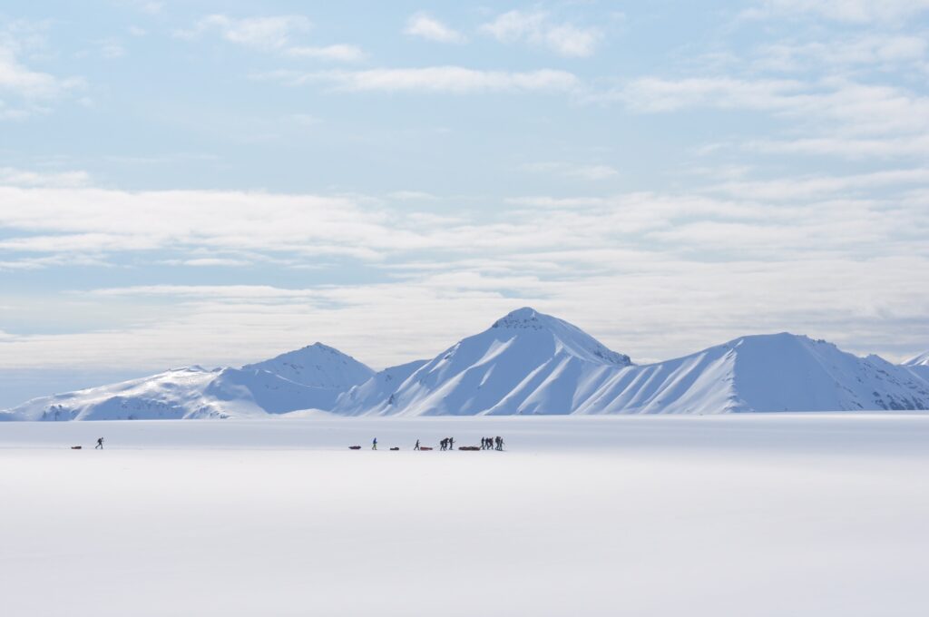 Ski expeditioners crossing an open snowfield in front of mountains.