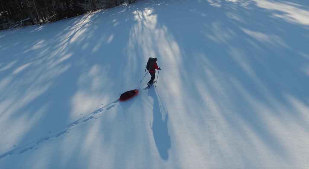 Aerial shot of Dianne snowshoeing with her sled behind her
