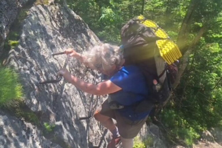 Betty climbing a metal ladder with her pack