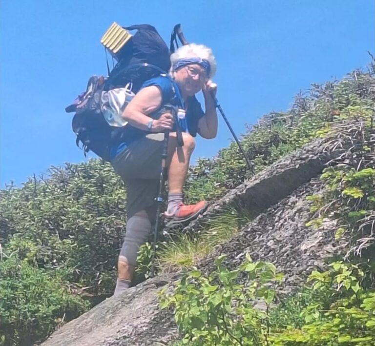 Betty with pack on her back climbing a steep hill